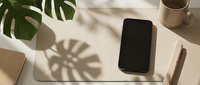 Modern workspace with smartphone on white desk featuring monstera plant shadow and coffee cup for productivity and lifestyle content.