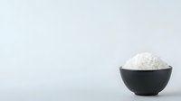 Minimalist composition of steamed white rice in black ceramic bowl against light background, emphasizing negative space and simplicity in food photography.