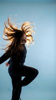 Young woman with flowing blonde hair dancing energetically against clear blue sky background. Dynamic movement captures freedom and joy in fitness lifestyle.