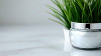 Fresh green grass plant in modern silver glitter pot on white marble surface, creating elegant home decor contrast.