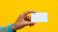 Hand holding blank white business card against bright yellow background for branding and marketing presentations.