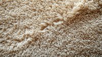 Soft beige carpet texture with dense pile creating luxurious plush surface. Close up macro view shows detailed fibers and natural wool-like appearance. Suitable for interior design.