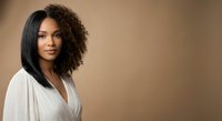 Professional mixed-race woman with curly hair in elegant white wrap top against warm beige background for business and lifestyle content.