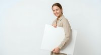 Young Caucasian businesswoman in beige blazer holding blank white poster against neutral background for marketing presentations and advertising mockups.