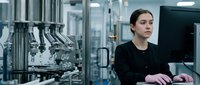 Young female scientist in black lab coat working with automated laboratory equipment in modern research facility for pharmaceutical development.
