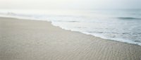 Serene sandy beach with gentle waves rolling onto shore, soft morning light creating peaceful coastal atmosphere for travel and relaxation content.