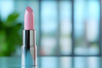 Pink lipstick in silver metallic case against blurred blue background with soft green plant element, ideal for beauty and cosmetic advertising.