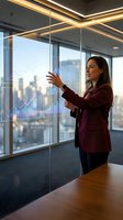 Professional businesswoman presenting financial data analytics on interactive glass display in modern corporate office with city skyline view.