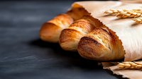 Freshly baked French baguettes wrapped in kraft paper with wheat ears on dark background, showcasing artisanal bread craftsmanship.