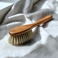 Natural wooden brush with soft bristles and long handle on white linen fabric background, minimalist eco-friendly cleaning tool for sustainable lifestyle.