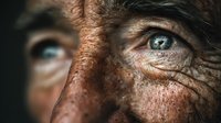 Close-up portrait of elderly man with weathered skin and piercing blue eyes showing wisdom and life experience through detailed facial wrinkles.