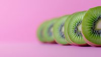 Fresh kiwi fruit slices arranged in row on pink background with selective focus, showing vibrant green flesh and black seeds. Minimal food photography.