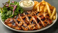 Grilled chicken breast sliced on white plate with french fries, fresh green salad and creamy sauce. Close up of juicy meat with charred grill marks and sides.