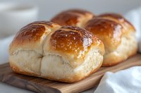 Freshly baked soft milk bread rolls with glossy golden brown top crust arranged on wooden cutting board, showing tender texture and buttery shine.