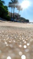 Sparkling sandy beach with palm trees and resort buildings in background, sunlight creating glittering bokeh effect on sand surface.