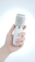 Hand holding white professional microphone with silver mesh grille on clean background for recording and broadcasting applications.