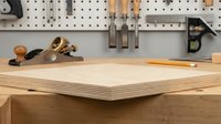 Woodworking workshop with plywood sheets on workbench and hand plane tools on pegboard wall. Carpentry workspace setup for furniture making projects.