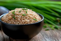Brown rice garnished with fresh chives in black ceramic bowl on rustic wooden table with green blurred background. Natural healthy eating concept.