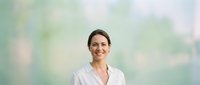 Young woman with brown hair and fair complexion wearing white blouse against soft blurred green and white background. Suitable for corporate, healthcare, wellness, and professional business applications.