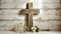 Wooden cross with white flowers on rustic weathered wood background for Easter celebration, religious ceremony, memorial service, spiritual decoration.