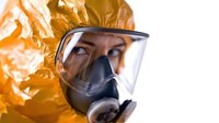 Person wearing protective hazmat suit and full-face respirator mask against orange background. Close-up portrait showing safety equipment for chemical or biological hazards.