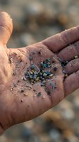 Cupped hands holding colorful microplastic particles and debris collected from beach sand, highlighting ocean pollution and environmental contamination concerns.