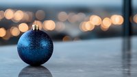 Blue glittery Christmas ornament ball on wooden surface with warm bokeh lights background creating festive holiday atmosphere for seasonal decorations.