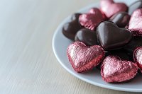 Pink and dark chocolate heart-shaped candies arranged on gray plate against light background, romantic holiday confectionery for Valentine's Day celebration.