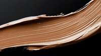 Smooth bronze makeup foundation cream smear stroke isolated on black background for cosmetic beauty product advertising and skincare campaigns.