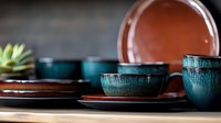 Handcrafted ceramic dinnerware set with teal glazed bowls and terracotta plates on wooden surface. Artisan pottery collection for modern dining and kitchen.
