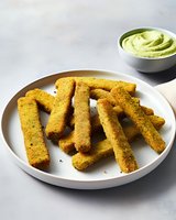 Crispy golden polenta sticks served on white plate with creamy avocado dip, perfect for appetizers or party snacks.