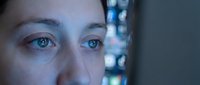 Close-up of a woman's face with blue eyes, illuminated by digital screen light, reflecting technology and digital connection for web, app, and tech industry use.