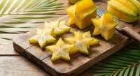 Fresh star fruit slices on wooden cutting board with tropical palm leaves. Exotic carambola pieces ready for healthy snacking and culinary preparation.