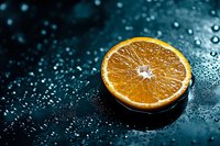 Fresh orange slice on dark wet surface with water drops and bokeh lights creating dramatic mood for food photography and healthy lifestyle concepts.