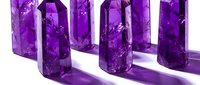 Purple amethyst crystal towers arranged in row casting shadows on white surface for meditation, healing, spiritual practices and gemstone collections.