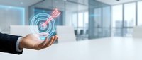 Businessman hand presenting glowing target with arrow hologram in modern office space representing goal achievement and business success strategy.