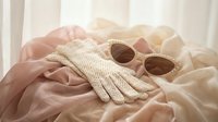 Elegant vintage lace gloves and round sunglasses on soft pink fabric creating romantic feminine fashion styling for luxury accessories photography.