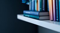Stack of books on white shelf against dark background with soft focus and blurred edges creating minimalist composition for reading and education concepts.
