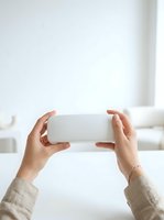 Female hands holding white rectangular product box in horizontal position against bright minimalist background for product showcase and packaging display.