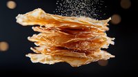 Crispy layered phyllo pastry sheets dusted with powdered sugar against dark background with bokeh lights, macro food photography showing delicate texture.