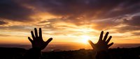 Two hands reaching toward golden sunset sky symbolizing hope, freedom, and spiritual connection in dramatic landscape silhouette for inspirational content.