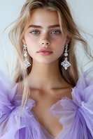 Young woman with blue eyes wearing crystal drop earrings and lavender tulle dress, natural makeup look with pink lips, blonde wavy hair styled casually for fashion portrait.