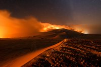 Dramatic desert landscape at night with glowing orange sky and illuminated sand dunes under starry night, creating ethereal atmosphere and otherworldly scenery.