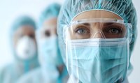 Healthcare professional in protective equipment with surgical mask, cap, and safety goggles during medical procedure in hospital setting.