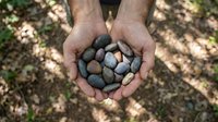 Hands cupping collection of smooth river stones and pebbles outdoors in natural sunlight for meditation, zen garden design, and wellness concepts.