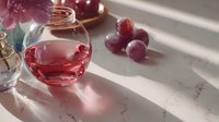 Red wine in round glass carafe with fresh grapes on marble surface, bathed in soft sunlight creating elegant shadows.