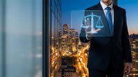 Professional businessman in suit touching digital justice scales hologram interface against urban city skyline at dusk for legal technology concepts.