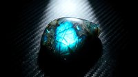 Glowing blue labradorite gemstone with iridescent flash on dark carbon fiber background showcasing natural mineral beauty and metaphysical properties.