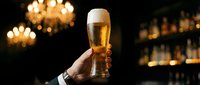 Hand holding a glass of golden beer against blurred bar background with warm lighting, suitable for beverage, hospitality, and celebration concepts.