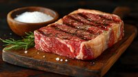 Juicy marbled raw beef steak on wooden cutting board with salt and rosemary, ready for grilling or cooking gourmet meals.